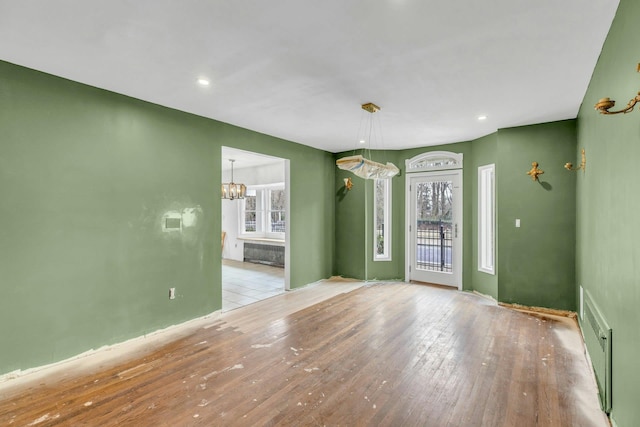 empty room featuring radiator heating unit, a chandelier, and light hardwood / wood-style flooring