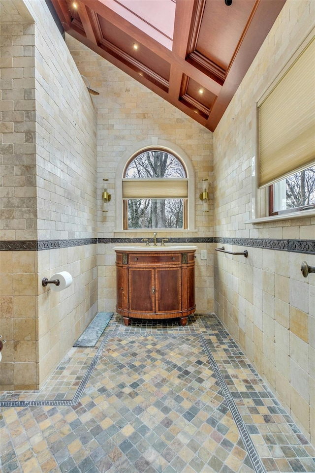 bathroom with coffered ceiling, tile walls, vanity, beam ceiling, and a high ceiling