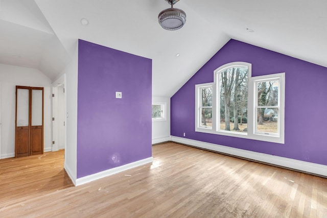 additional living space with a baseboard radiator, vaulted ceiling, and light wood-type flooring