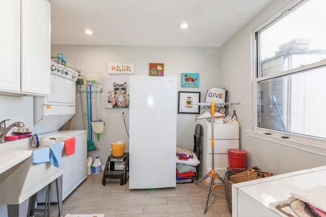 kitchen featuring sink, light hardwood / wood-style flooring, stacked washing maching and dryer, white cabinetry, and white refrigerator