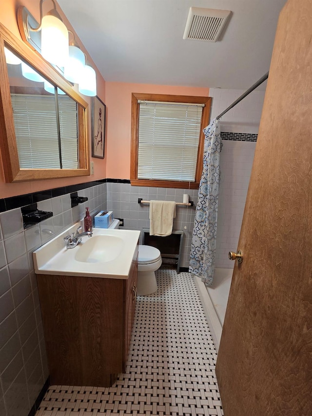 bathroom featuring walk in shower, vanity, toilet, and tile walls