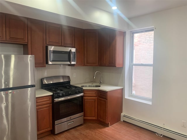 kitchen with sink, baseboard heating, appliances with stainless steel finishes, light hardwood / wood-style floors, and backsplash