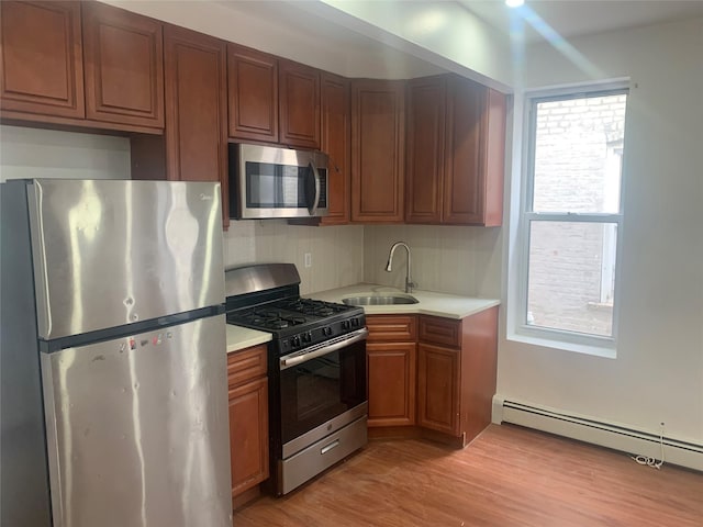 kitchen with a baseboard radiator, appliances with stainless steel finishes, sink, and light wood-type flooring