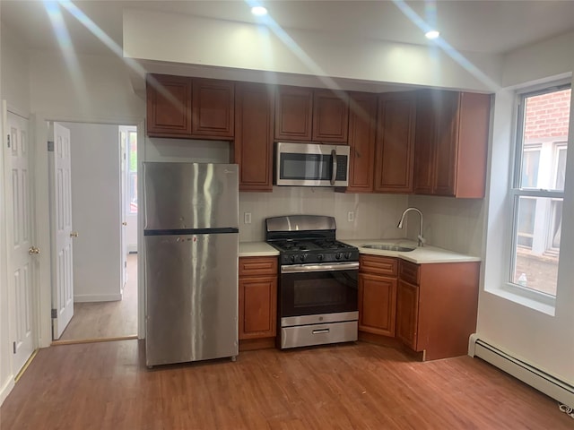 kitchen with sink, light hardwood / wood-style flooring, appliances with stainless steel finishes, tasteful backsplash, and a baseboard radiator