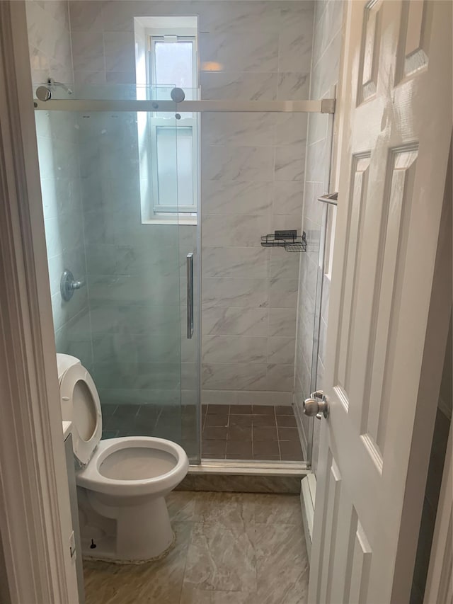 bathroom featuring a shower with door and toilet