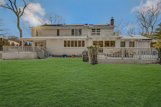 back of property with solar panels, a deck, and a lawn