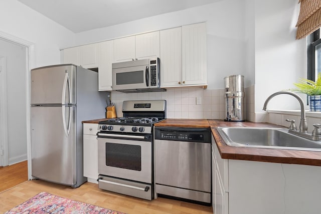 kitchen with butcher block countertops, sink, stainless steel appliances, white cabinets, and light wood-type flooring