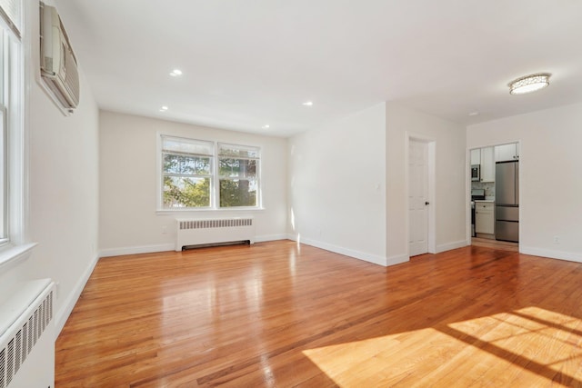 unfurnished living room featuring radiator, light hardwood / wood-style floors, and a wall mounted AC