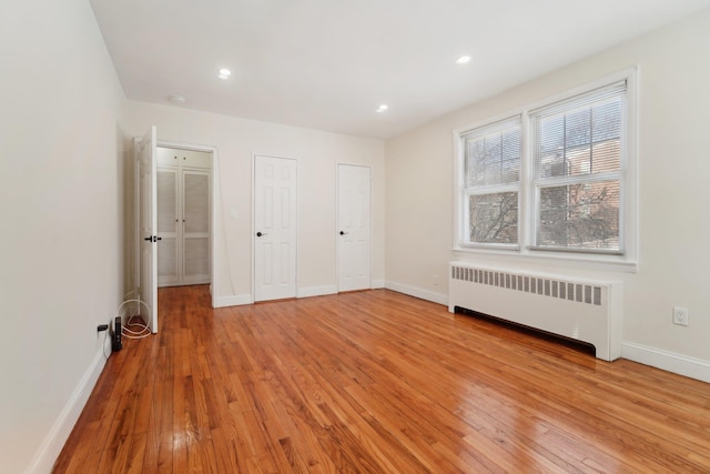 unfurnished bedroom with multiple closets, radiator heating unit, and light hardwood / wood-style flooring