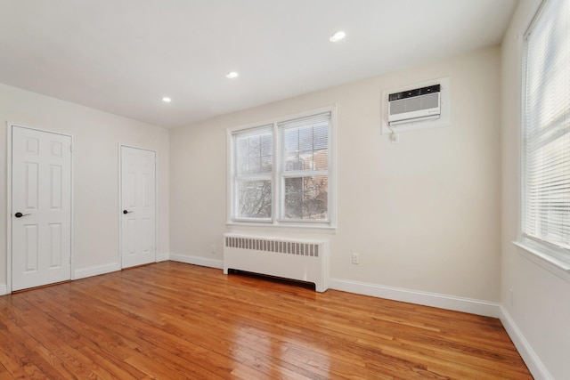 unfurnished bedroom featuring radiator heating unit, an AC wall unit, and light wood-type flooring