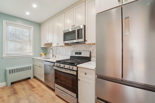 kitchen featuring sink, radiator, stainless steel appliances, light hardwood / wood-style floors, and white cabinets