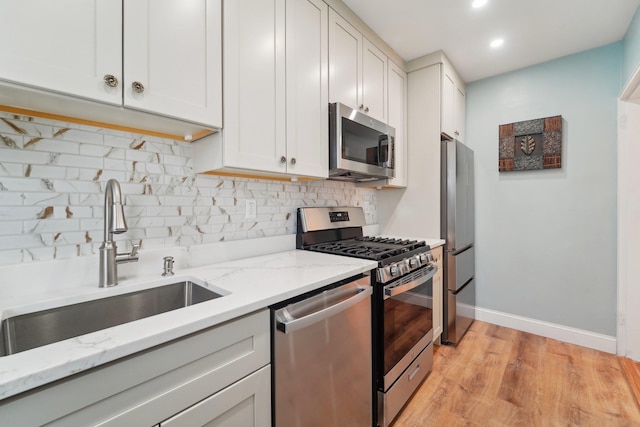 kitchen featuring appliances with stainless steel finishes, sink, backsplash, white cabinets, and light stone counters