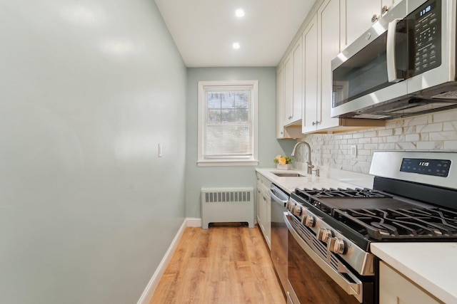 kitchen with radiator heating unit, white cabinetry, sink, light hardwood / wood-style floors, and stainless steel appliances