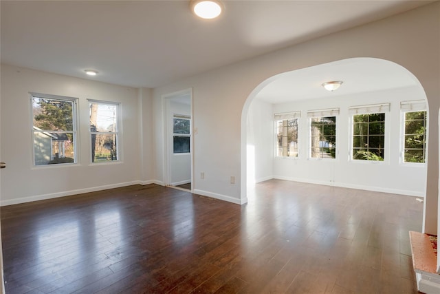 unfurnished room with arched walkways, baseboards, and dark wood-type flooring