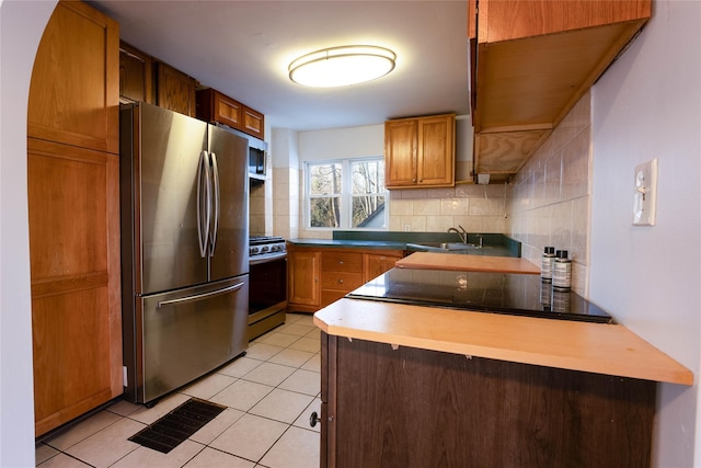 kitchen featuring backsplash, brown cabinetry, stainless steel appliances, and a sink