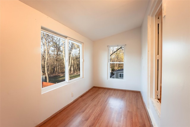 spare room featuring light wood-style flooring, lofted ceiling, and baseboards
