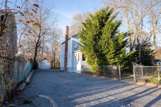 view of side of property with a chimney, aphalt driveway, fence, an outbuilding, and a garage