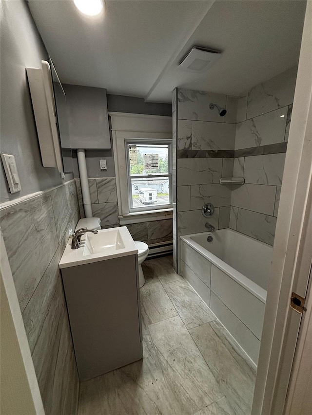 full bathroom featuring tiled shower / bath, vanity, toilet, and tile walls