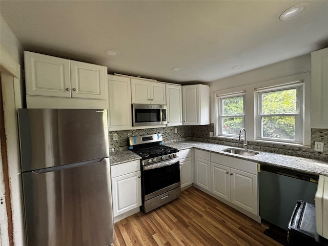 kitchen with sink, appliances with stainless steel finishes, white cabinetry, wood-type flooring, and decorative backsplash