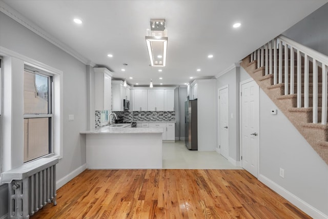 kitchen with radiator, crown molding, appliances with stainless steel finishes, white cabinets, and kitchen peninsula