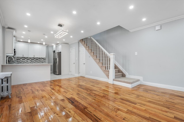 unfurnished living room with sink, light hardwood / wood-style flooring, and ornamental molding