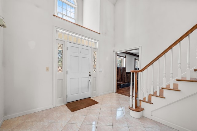 foyer with a towering ceiling, light tile patterned floors, baseboards, and stairway