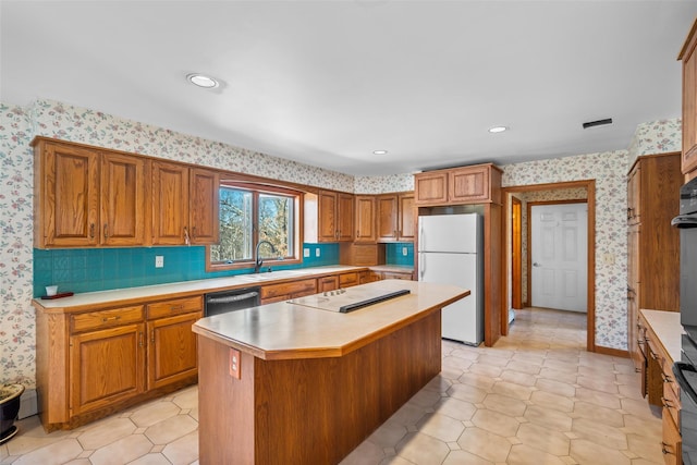 kitchen with a sink, light countertops, freestanding refrigerator, dishwasher, and wallpapered walls