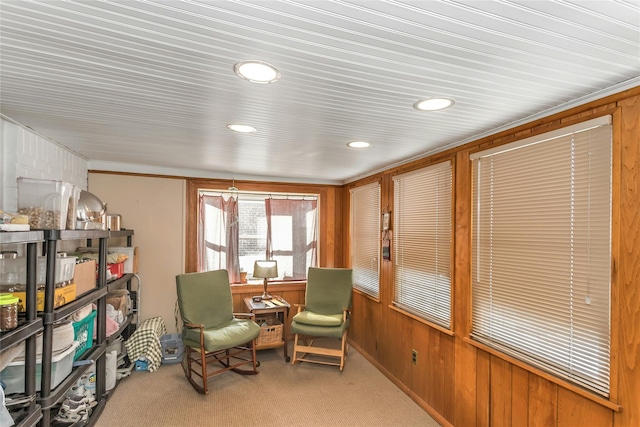 living area featuring ornamental molding, wooden walls, and light colored carpet