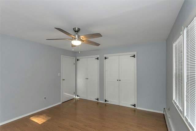 unfurnished bedroom with multiple closets, ceiling fan, dark hardwood / wood-style floors, and a baseboard radiator