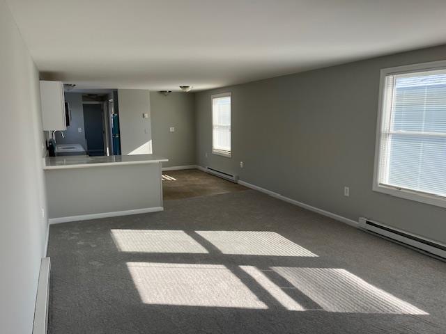 unfurnished living room with dark colored carpet, a healthy amount of sunlight, sink, and a baseboard heating unit