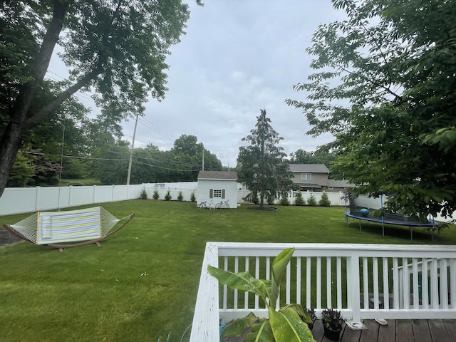 view of yard featuring a trampoline, a wooden deck, and an outdoor structure