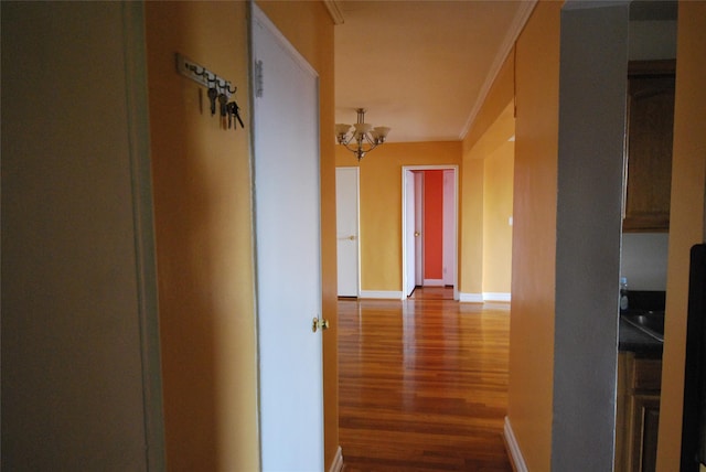 hallway with an inviting chandelier, crown molding, and wood-type flooring