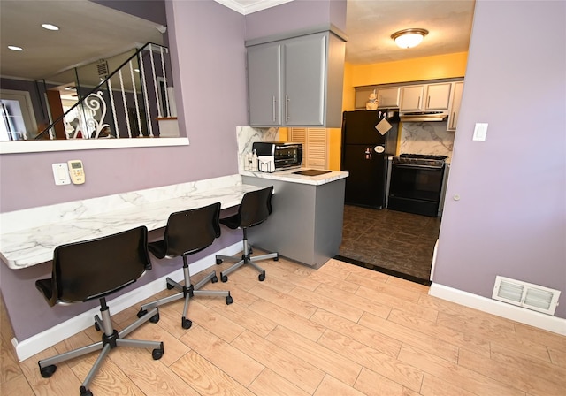 kitchen with a breakfast bar, black refrigerator, gray cabinets, gas range oven, and decorative backsplash