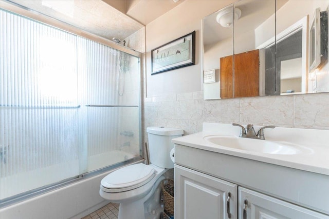 full bathroom with combined bath / shower with glass door, tile walls, vanity, toilet, and tile patterned floors