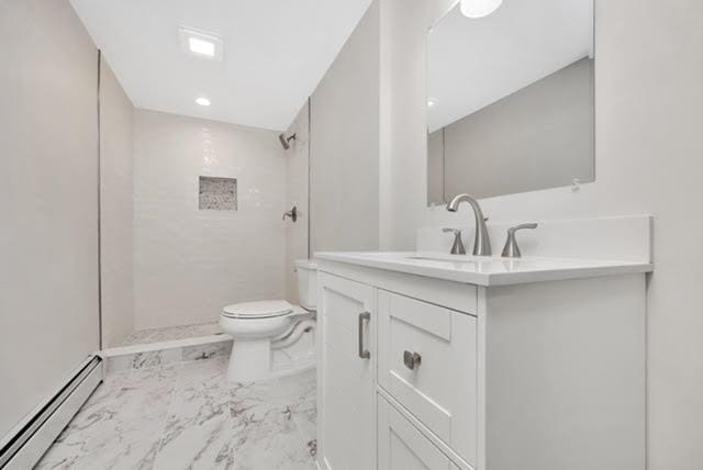 bathroom featuring vanity, a baseboard heating unit, toilet, and tiled shower