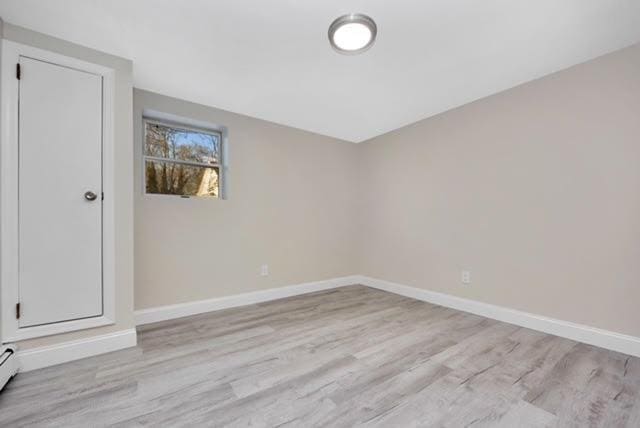 unfurnished room with a baseboard heating unit and light wood-type flooring