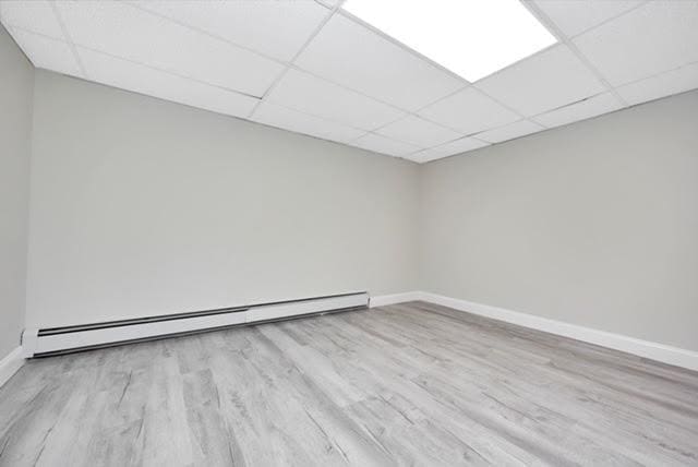 empty room with a baseboard heating unit, a paneled ceiling, and light hardwood / wood-style flooring