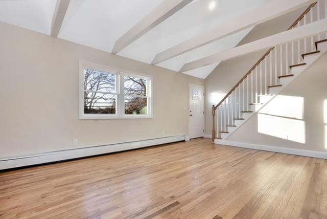 interior space with lofted ceiling with beams, wood finished floors, baseboards, baseboard heating, and stairs