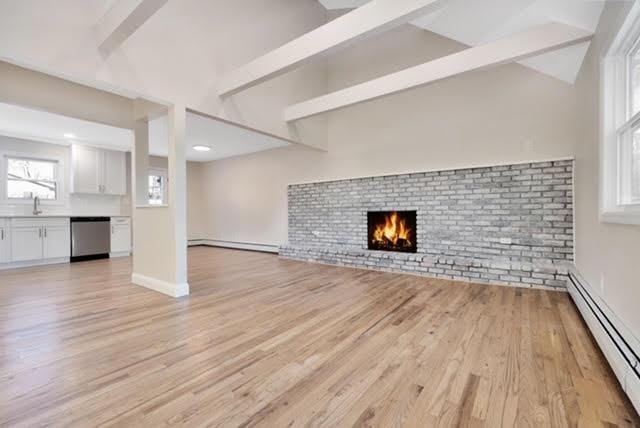 122 Vernon Valley Rd, East Northport, NY 11731 - unfurnished living room featuring lofted ceiling with beams, light wood-type flooring, baseboard heating, and a brick fireplace