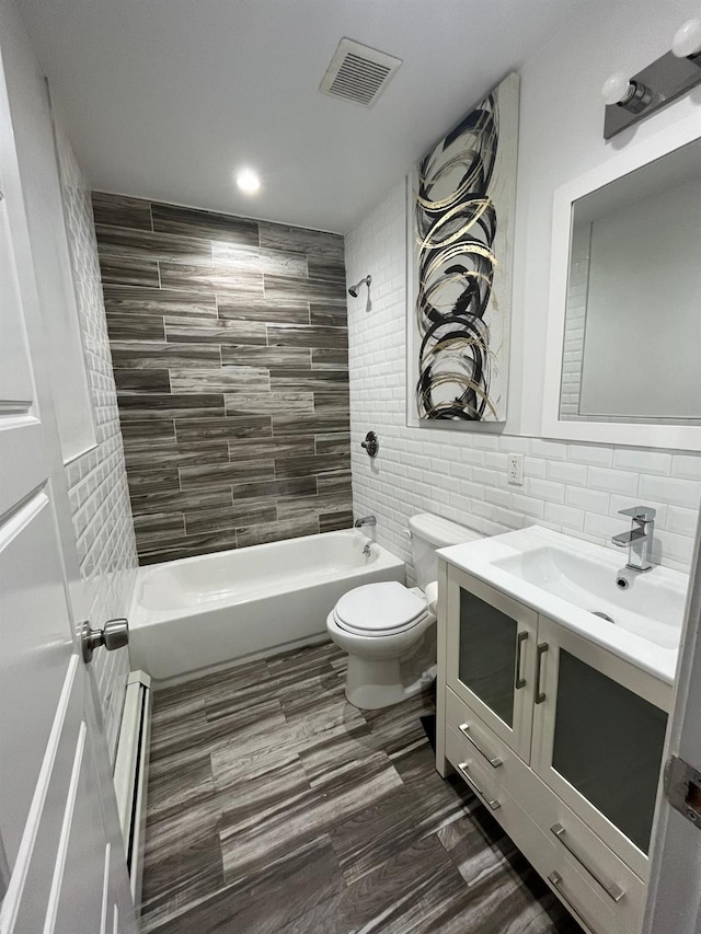 full bathroom featuring toilet, tile walls, vanity, tiled shower / bath combo, and a baseboard heating unit