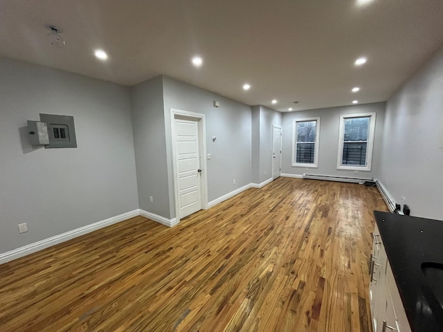 unfurnished living room featuring wood-type flooring, electric panel, and a baseboard heating unit