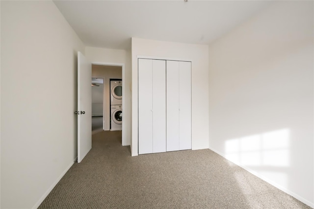 unfurnished bedroom with stacked washer / drying machine, a closet, and dark colored carpet