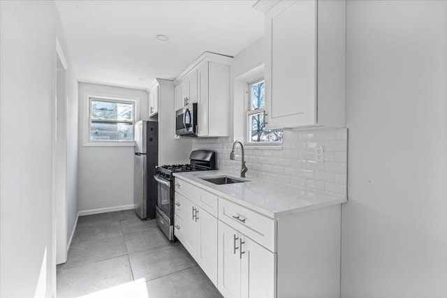 kitchen with appliances with stainless steel finishes, tasteful backsplash, white cabinetry, sink, and light stone countertops