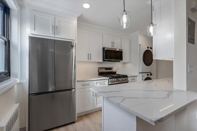 kitchen with white cabinetry, appliances with stainless steel finishes, radiator, stacked washing maching and dryer, and backsplash