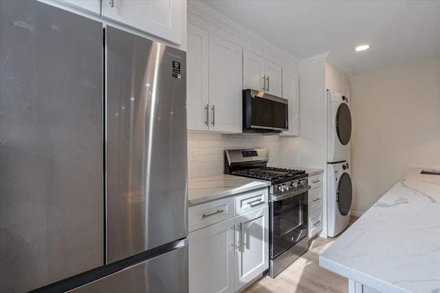 kitchen featuring white cabinetry, light stone countertops, stacked washer and clothes dryer, and appliances with stainless steel finishes