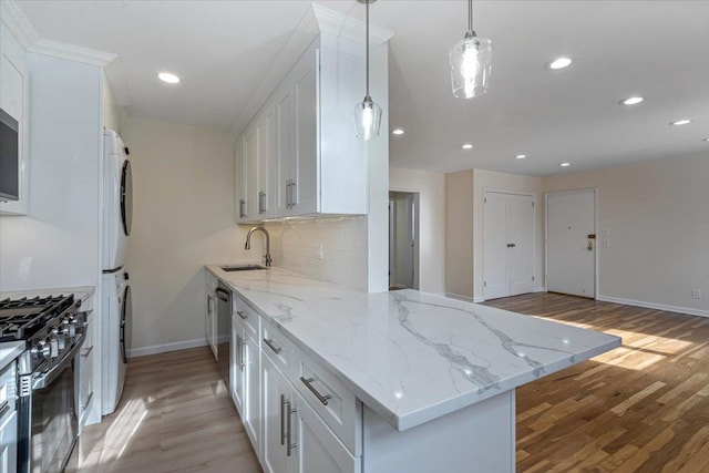 kitchen featuring stacked washer and clothes dryer, range with gas cooktop, white cabinetry, light stone counters, and kitchen peninsula