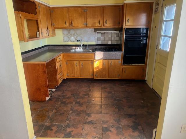 kitchen with black double oven, range hood, sink, and decorative backsplash