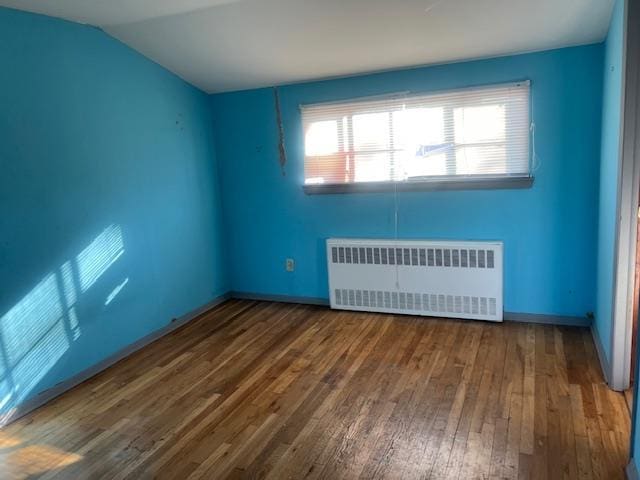 spare room with lofted ceiling, radiator, and hardwood / wood-style floors