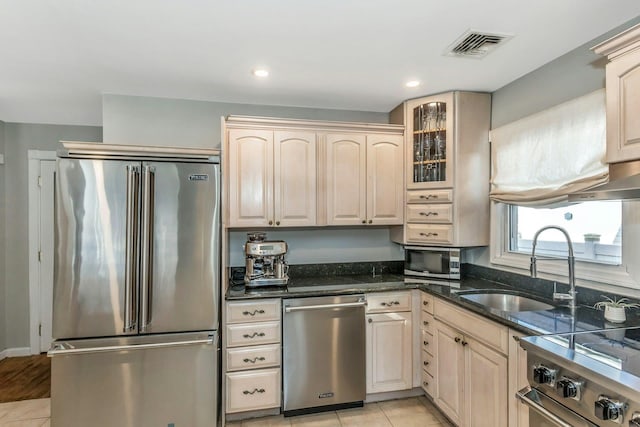 kitchen with high end appliances, dark stone counters, light tile patterned flooring, and sink