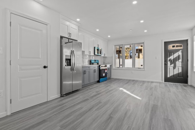 kitchen with white cabinetry, backsplash, light hardwood / wood-style flooring, and appliances with stainless steel finishes